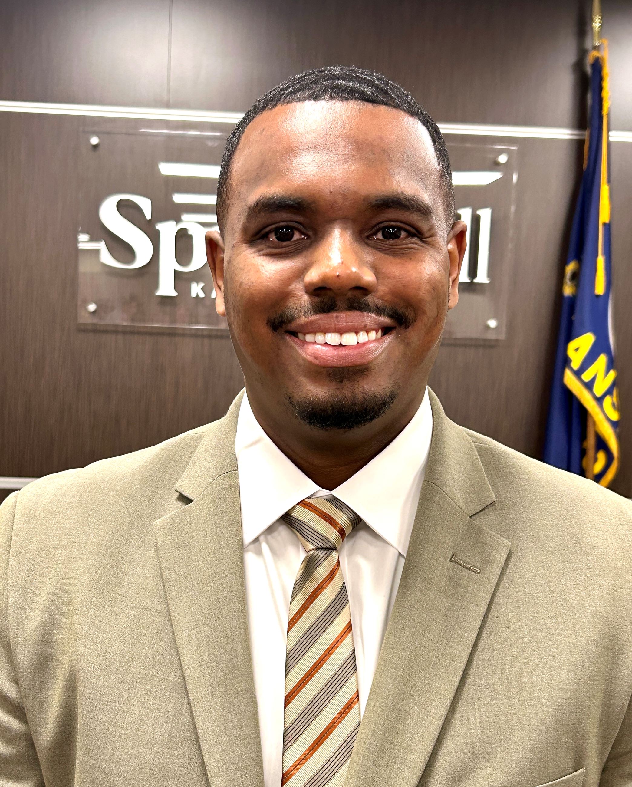 Headshot of a man wearing a tan suit. 